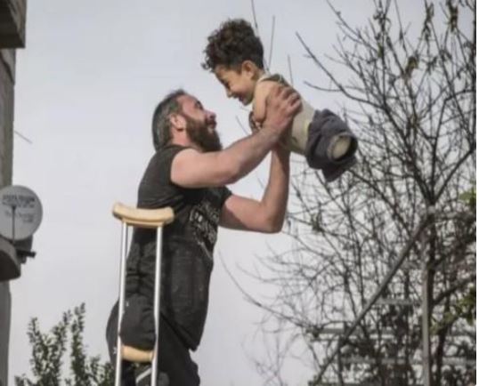 ظهر طفله دون أطراف.. تفاصيل قصة صورة السوري المعاق وابنه التي أثارت تعاطف العالم -فيديو